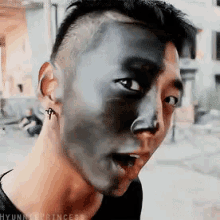 a man with black paint on his face is making a funny face with his mouth open .