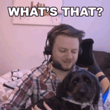 a man wearing headphones is holding a small black dog and says what 's that ?