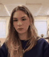 a woman wearing a blue sweater and a cross necklace looks at the camera .