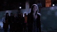 a woman in a black jacket is standing in front of a crowd of people