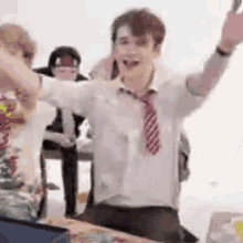 a man in a white shirt and red tie is standing in front of a table with his arms in the air .