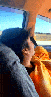 a man sleeping in a car with an orange blanket