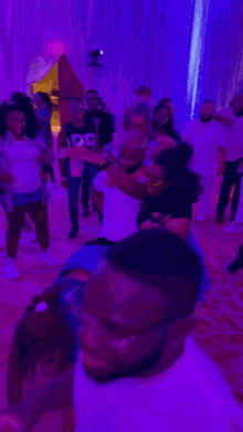 a group of people are dancing in a room with purple lights and one of them is wearing a shirt with the number 99 on it
