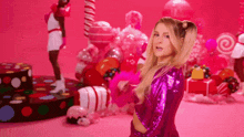 a woman in a purple outfit is standing in front of a pink background with balloons and lollipops .