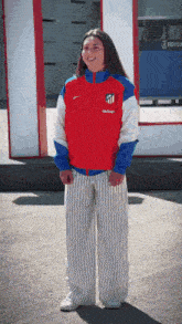 a woman wearing a red jacket and striped pants is standing in front of a sign that says 3r