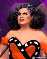a drag queen is wearing a black and orange dress with a heart on it