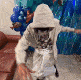 a person in a hoodie is dancing in front of balloons and a couch