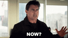 a man in a black jacket says " now " in front of a window