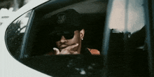 a man wearing a hat and sunglasses is driving a white car
