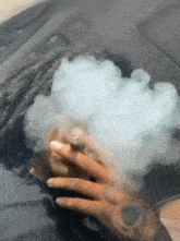 a woman with dreadlocks is smoking a cigarette in a car with smoke coming out of her mouth .