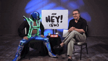 a man sits in front of a sign that says hey ew