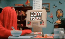 a cartoon character is sitting at a desk with a computer monitor that says do n't touch .