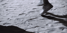 a person walking on a sandy beach with their shadow on the ground