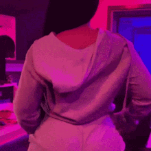 a woman wearing a white hoodie is sitting in front of a pink wall
