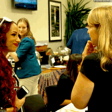 a woman holding a cell phone talks to another woman in a room
