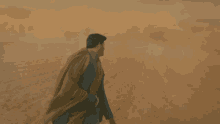 a man in a suit and cape is walking through a desert