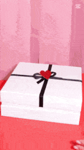 a white box with a black ribbon and a red heart on it is on a red table .