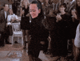 a woman in a black dress is dancing in front of a crowd of people at a party .