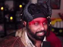 a man with a beard and red paint on his face is wearing a headband with horns on it .