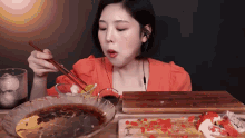 a woman is eating a bowl of food with chopsticks and a cutting board that says ' mixed ' on it