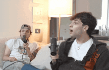 two men are sitting on a couch one is holding a microphone and the other is wearing a hoodie that says off white
