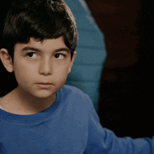 a young boy is wearing a blue shirt and looking at the camera