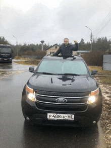 a man stands on the roof of a black ford car
