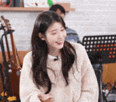 a woman wearing a white sweater and a microphone smiles while sitting on a chair