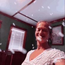 a woman in a white dress is smiling in front of a window with blinds on it