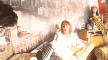 a woman with red hair is smoking a cigarette in front of a wall with a picture of new york city