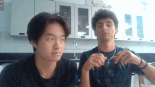 a man wearing a necklace with a cross on it is sitting next to another man