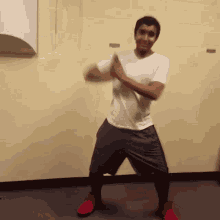 a man in a white shirt is dancing in front of a wall
