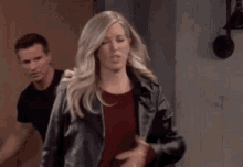a man and a woman are standing next to each other in a room . the woman is wearing a leather jacket .