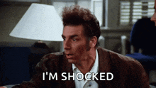 a man is sitting at a table with a lamp and says `` i 'm shocked '' .
