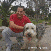 a man in a red shirt kneeling down next to a small dog