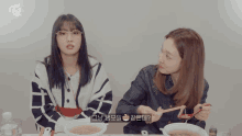 two women are sitting at a table with a bowl of soup and a bottle of water with the letters twice on it