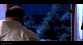 a man in a white shirt is looking out of a window at night