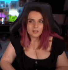 a woman with pink hair is sitting in a gaming chair and looking at the camera .