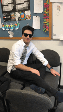 a man wearing sunglasses sits on a chair in front of a board with a calendar for 2017