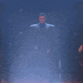 a man in a suit is dancing on a stage in front of a blue wall