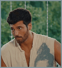 a man with a beard and a sleeveless shirt is looking at the camera .