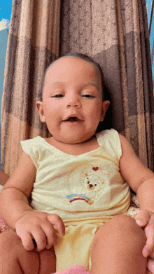 a baby wearing a yellow tank top with a teddy bear embroidered on it