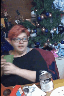 a woman with red hair is sitting in front of a christmas tree holding a card
