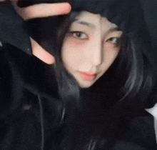a girl is wearing a black hoodie and making a heart with her hands .