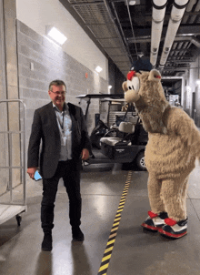 a man in a suit stands next to a mascot in a hallway