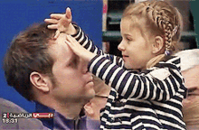 a little girl putting her hand on a man 's forehead with the time 18:37 on the bottom