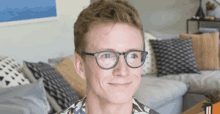 a man wearing glasses is smiling in front of a couch with pillows