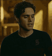 a young man with curly hair is wearing a black sweater with a snake on the back .