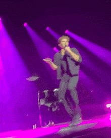 a man singing into a microphone on stage with purple lights behind him