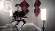 a man is playing a guitar in a room with a r on the wall